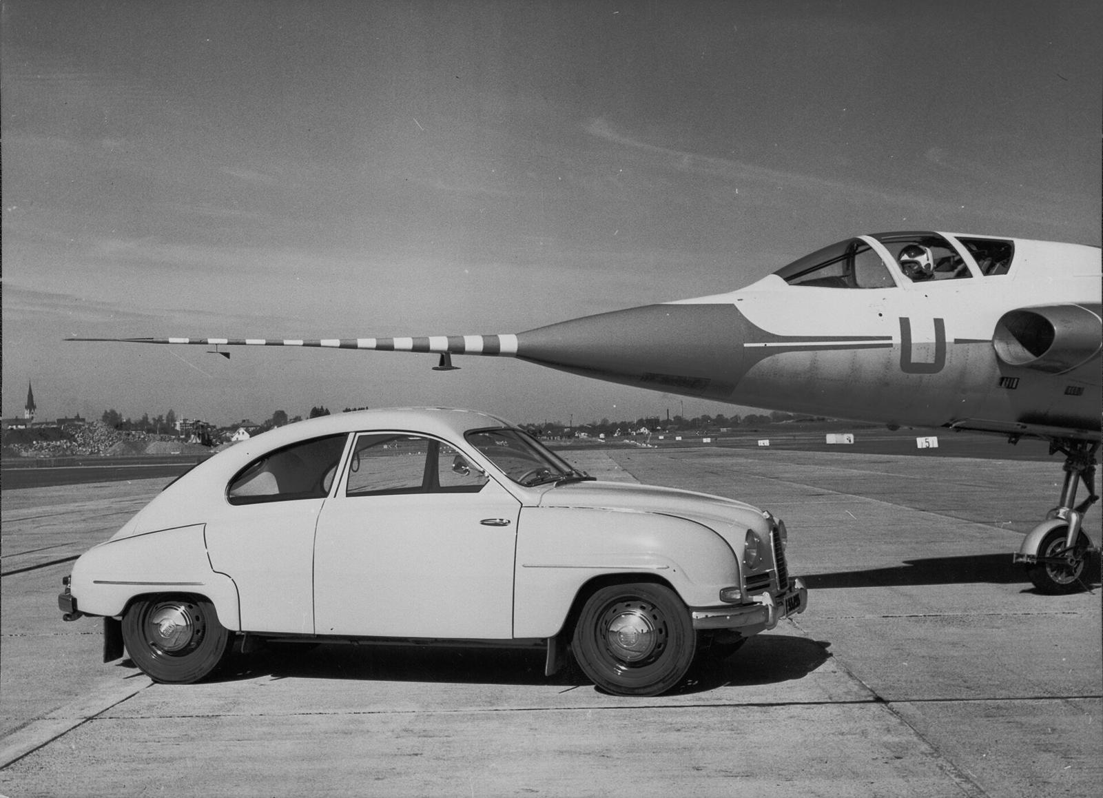 Svart-hvitt pressebilde av en Saab 93B på en flystripe, foran et jagerfly