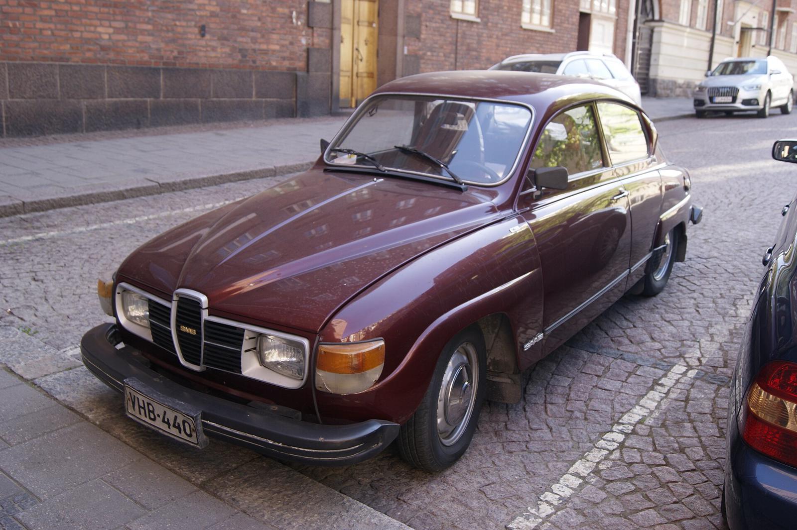 Vinrød Saab 96 V4 med store svarte støtfangere parkert på brostein
