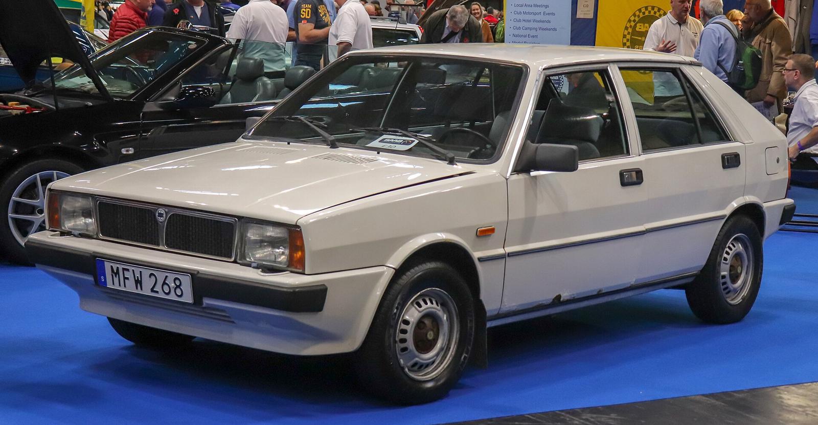 Hvit Saab-Lancia 600 GLS sett skrått forfra på en innendørs bilutstilling