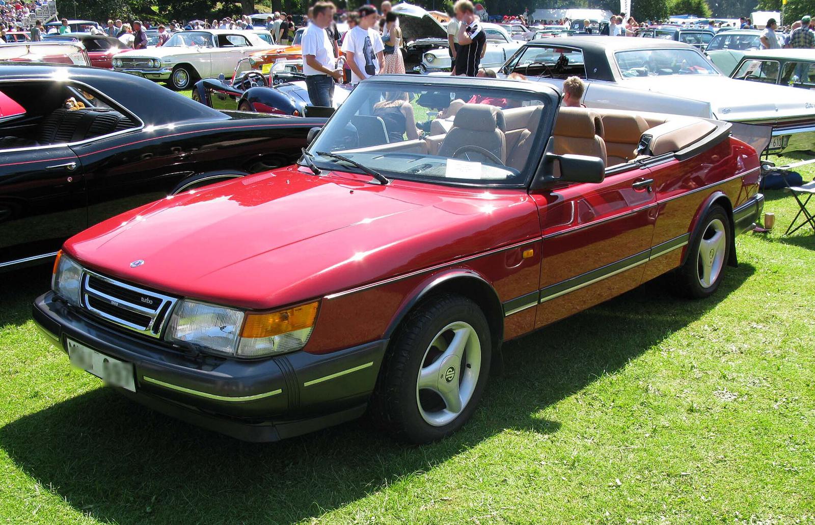 Rød Saab 900 Turbo Cabriolet med nedfelt kalesje og lys skinninteriør på en gressplen
