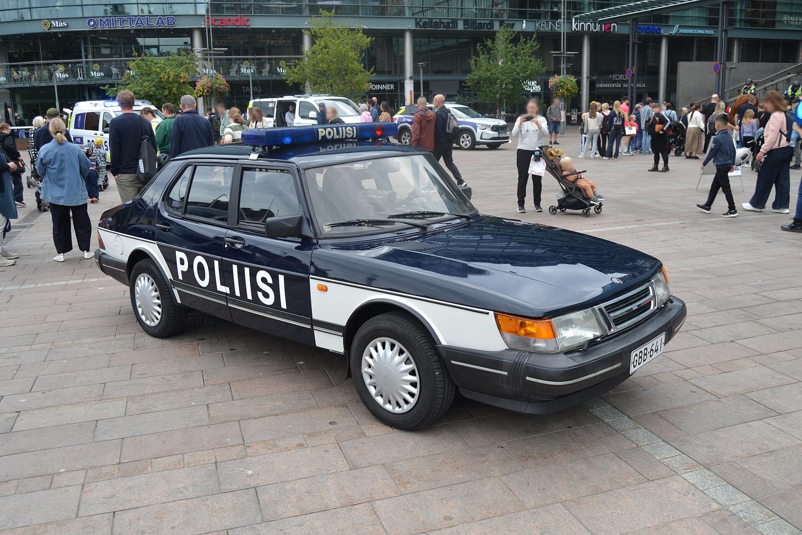 Mørkeblå og hvit Saab 900i sedan med POLIISI-dekor på et torg