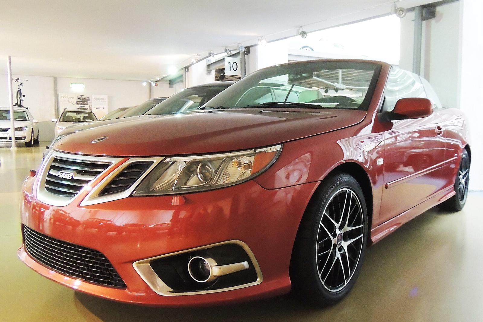 Oransje metallic Saab 9-3 cabriolet med kalesjen oppe, sett skrått forfra i et utstillingslokale