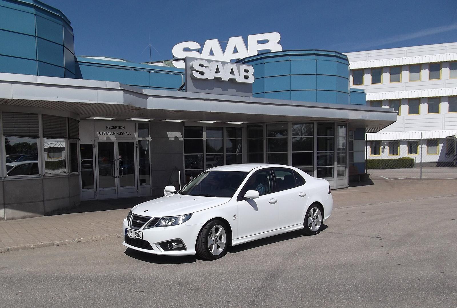 Hvit Saab 9-3 Griffin sedan parkert foran inngangen til Saab-fabrikken i Trollhättan, med Saab-skilt på bygget