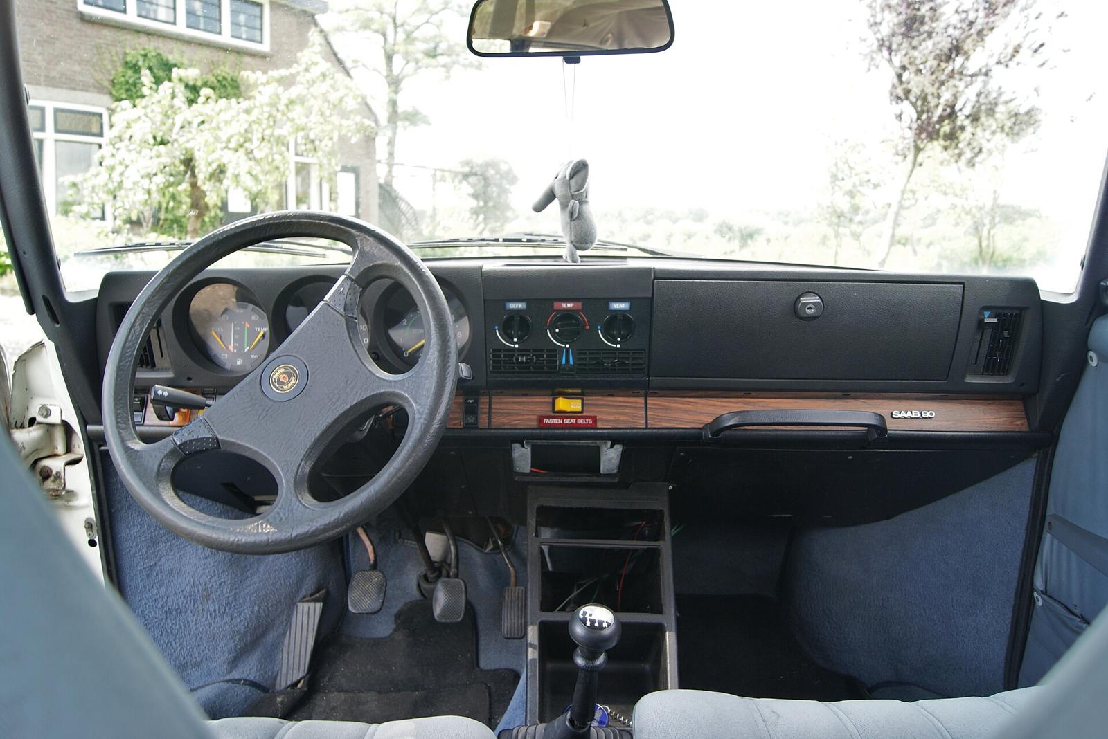Førerplassen i en Saab 90 med firekjeret ratt og mørkt dashbord med trelist