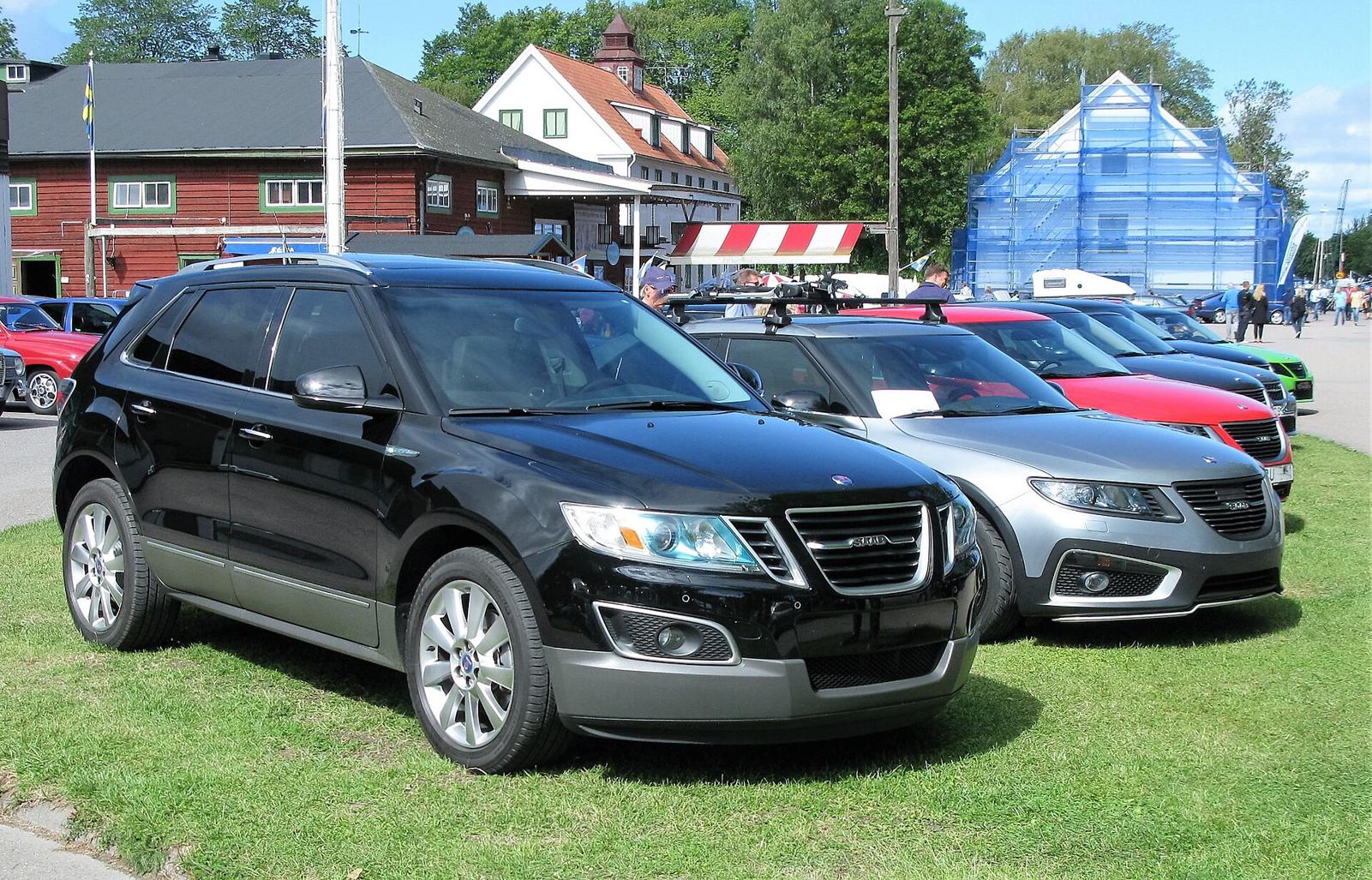Svart Saab 9-4X på en gressplen foran en sølvfarget Saab 9-5 og flere Saab-biler