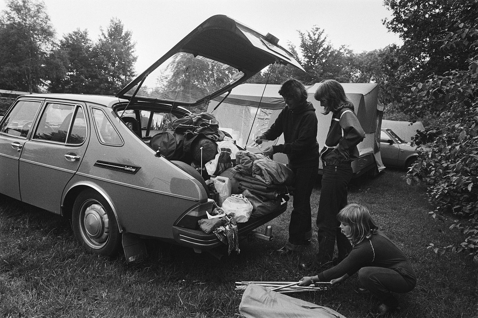 Svart-hvitt bilde av en familie som pakker bagasje i en Saab 99 Combi Coupé med åpen bakluke