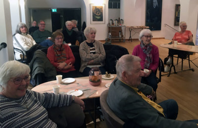 Eldre mennesker sitter rundt bord og lytter til foredrag.